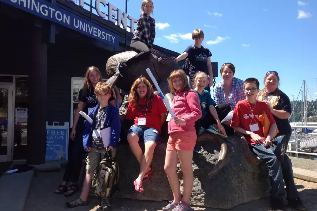 A group of students stand outside the sea discovery center around a sculpture looking enthusiastic