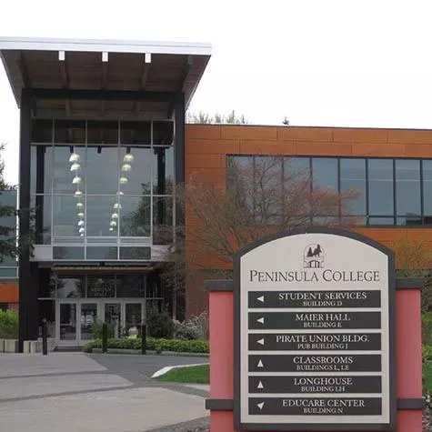 A modern glass and wood building with a prominent Peninsula College sign in front of it.